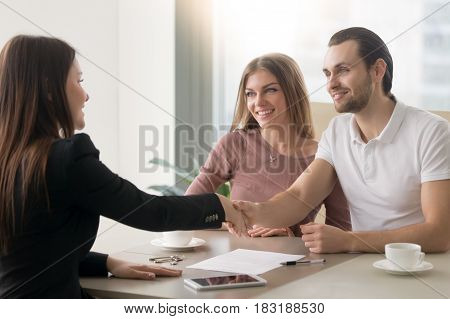 Meeting with agent in office, buying renting apartment or house, buyers of real estate ready to conclude a deal, family couple shaking hands with realtor after signing documents for realty purchase