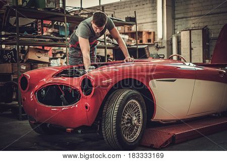 Mechanic working on classic car electrics in restoration workshop