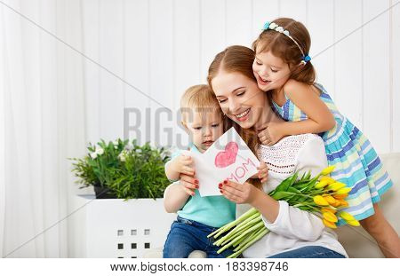 Happy mother's day! Children congratulates moms and gives her a postcard and flowers tulips