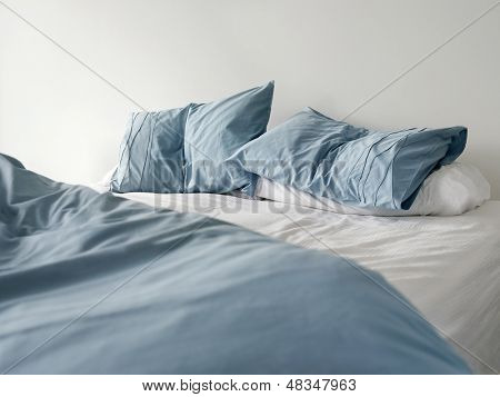 Morning view of an unmade bed with crumpled blue bed linens and no people