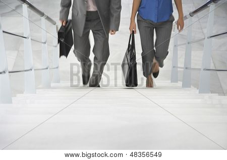 Lowsection of two businesspeople walking up stairs with bags in office