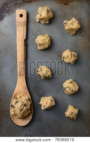 Overhead shot of chocolate chip cookie dough on a cookie sheet, with a wooden spoon holding a big gob of the raw dough. Vertical Format.