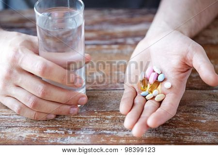 healthy lifestyle, medicine, nutritional supplements and people concept - close up of male hands holding pills with cod liver oil capsules and water glass