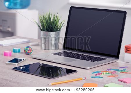 Modern office workplace with laptop computer mockup, tablet pc and smartphone on the office desk. There is a laptop, tablet computer, smartphone on the table. For design presentation or portfolio.