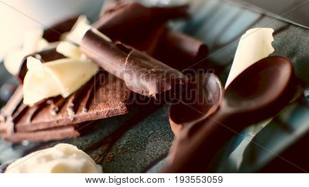 Rich Chocolate dessert photography with chocolate square cookie draped in chocolate and fudge sauce, with white chocolate curls and dark chocolate shavings and chocolate spoons for coffee or dessert conceptual background