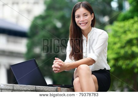 Business people - woman on laptop in Hong Kong. Businesswoman on computer and internet outside in Central Hong Kong. Young female professional business woman smiling. Asian Chinese Caucasian woman.