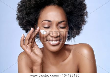 Beautiful black african model with flawless skin smooth complexion applying moisturiser face cream to her cheek, beauty cosmetics skincare concept