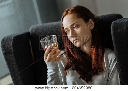 Alcohol addiction. Pleasant sad unhappy woman holding a glass of whisky and drinking it while being alcohol addicted