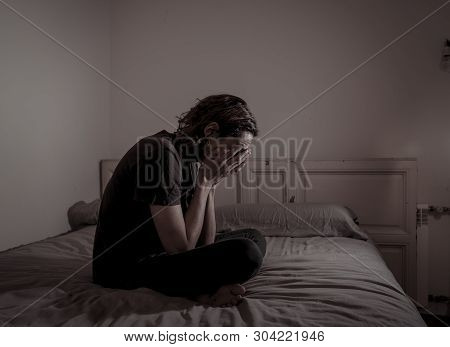 Desperate Lonely Teenager Man Suffering From Depression Sitting Alone On Bed