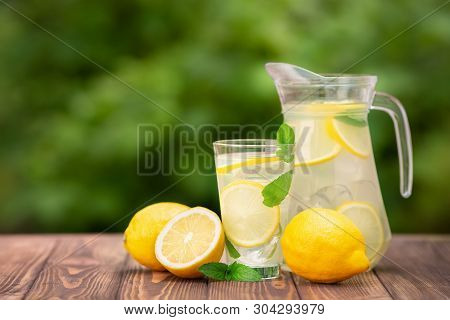 Lemonade In Glass And Jug On Wooden Table Outdoors. Summer Refreshing Drink. Cold Detox Water With L