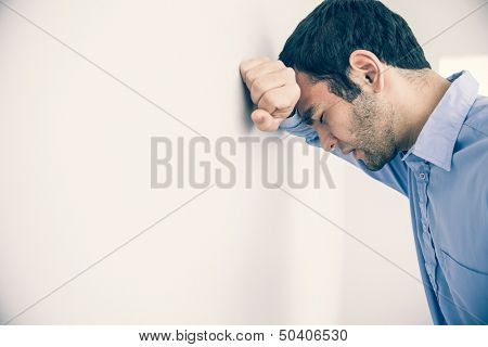 Depressed man with fist clenched leaning his head against a wall