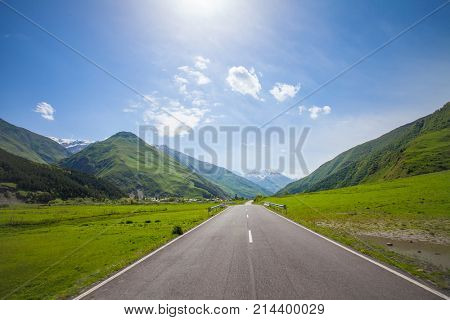 Mountain empty road with green hills and blue sunny sky. Mountains of the Caucasus, gorges, clouds, a narrow road, high mountains - all this is the military Georgian road.