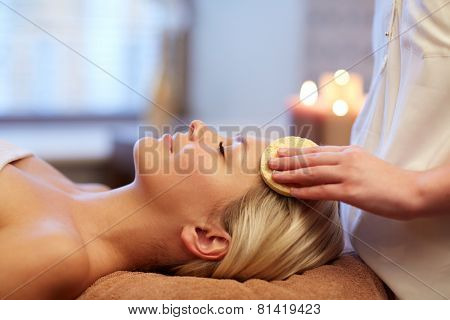 people, beauty, spa, healthy lifestyle and relaxation concept - close up of beautiful young woman lying with closed eyes and having face massage with sponge in spa