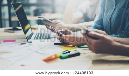 Team coworking process. Photo young business crew working with new startup project.Notebook on wood table. Using modern smartphones, typing message, analyze plans. Blurred background, film effect.