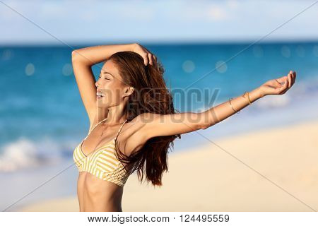 Carefree freedom joy bikini woman happy on beach feeling free with arms up at sunset on ocean background. Portrait of sexy body Asian girl smiling for skincare or weight loss concept.