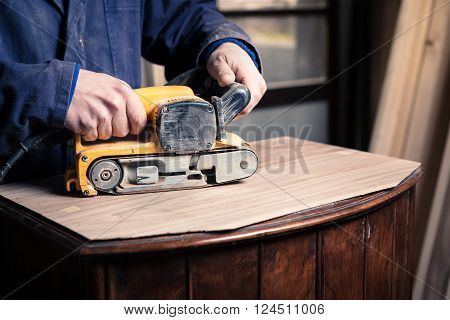 Carpenter Restoring Furniture With Belt Sander