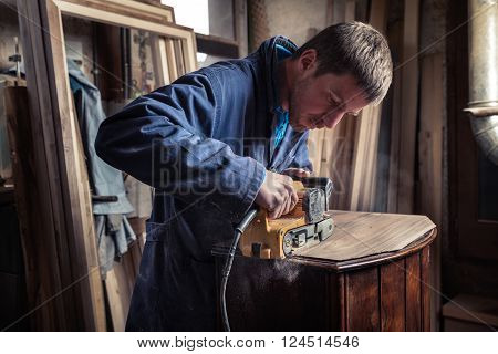 Carpenter Restoring Furniture With Belt Sander