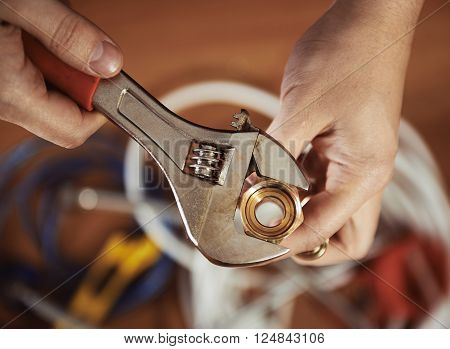 Close-up of plumber hands screwing nut of pipe with wrench over plumbing tools background. Concept of repair and technical assistance.