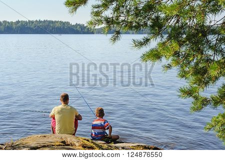 Father and son lake fishing together. They're using telescopic fishing rods fishing line floats and baited fishing hooks. Man has tattoos.