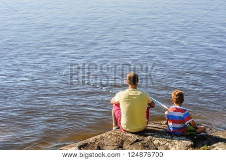 Father and son lake fishing together. They're using telescopic fishing rods fishing line floats and baited fishing hooks. Man has tattoos.