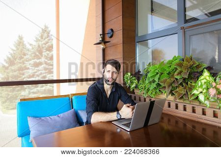 Educational consultant talking to student by laptop video call with headset microphone. Handsome serious man has beard and wears black shirt. Concept of assisting students in making decisions and giving advices in tuition fees, visa, and enrolling at High