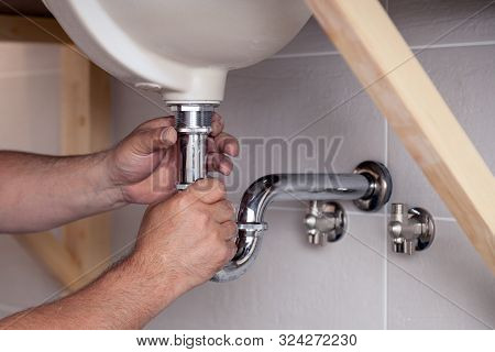 Closeup Male Plumber Worker In Blue Denim Uniform, Overalls, Fixing Sink In Bathroom With Tile Wall.