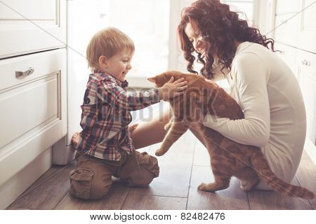 Mother with her baby playing with pet on the floor at the kitchen at home