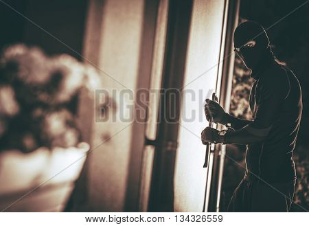 Home Burglar in a Mask Breaking Into the House. House Thief Concept Photo.