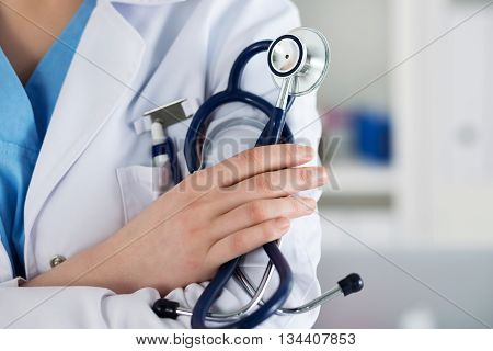 Closeup of female medicine therapeutist doctor standing with hands crossed on her chest holding stethoscope in office. Medical help or insurance concept. Physician is waiting for patient to examine