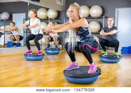 Dedicated people in workout team doing squats on half ball in a fitness gym class. Core muscle and balance workout. Teamwork and motivation.