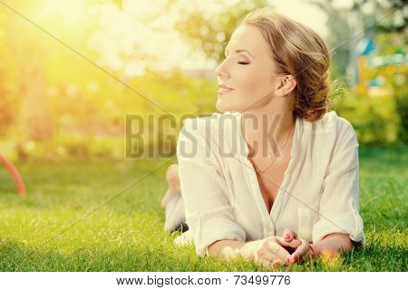 Beautiful smiling woman lying on a grass outdoor. She is absolutely happy. 