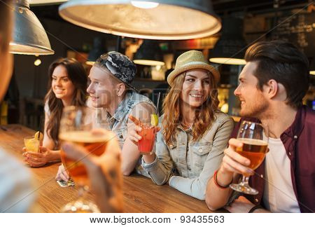 people, leisure, friendship and communication concept - group of happy smiling friends drinking beer and cocktails talking at bar or pub