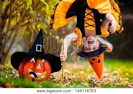 Little girl in witch costume playing in autumn park. Child having fun at Halloween trick or treat. Kids trick or treating. Toddler kid with jack-o-lantern. Children with candy bucket in fall forest.