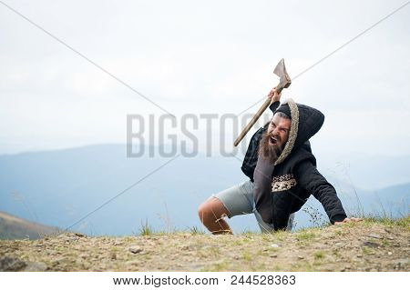 Man With Beard On Shouting Face Conquers Top Of Mountain With Axe, Sky Background. Survive In Wild N