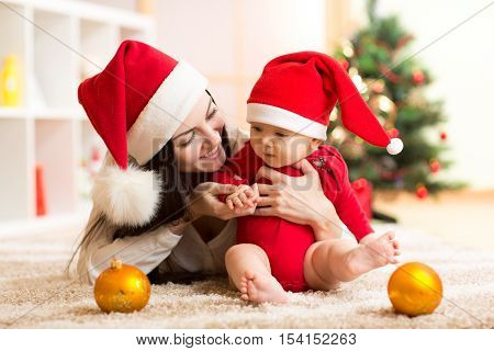 Mother and baby in santa red dress smile on a background of Christmas trees in the interior of the house