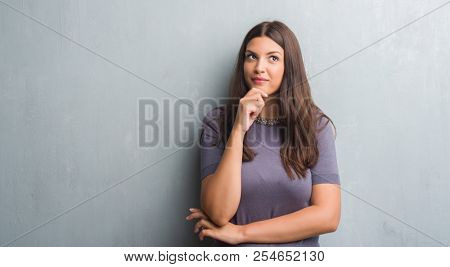 Young brunette woman over grunge grey wall serious face thinking about question, very confused idea