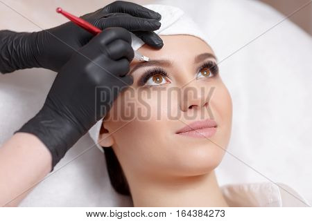 Permanent makeup eyebrows. Mikrobleyding eyebrows workflow in a beauty salon. Cosmetologist applying a special permanent makeup on a woman's eyebrows.