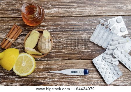 Ginger lemon honey and different drugs with thermometer on wooden background.Alternative remedies and traditional pills to treat colds and flu. Natural medicine vs conventional medicine concept.