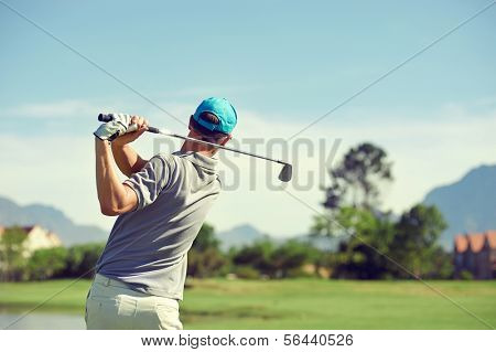 Golfer hitting golf shot with club on course while on summer vacation