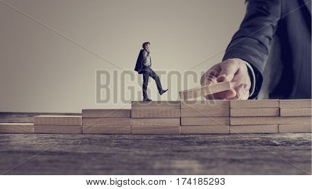 Retro vintage style image of a business person walking up steps while the hand of other man building stairs for him in a conceptual image of personal and career promotion leadership and opportunity.