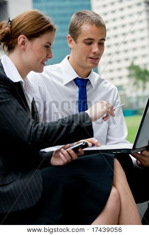 Two young business professionals sitting outside with a laptop computer