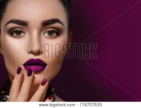 Beauty Brunette Woman with Perfect dark Makeup. Beautiful Professional Holiday Make-up. Deep violet color of Lips and Nails, perfect eyebrows. Beauty Girl's Face isolated on burgundy color background