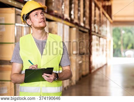 Portrait white caucasian warehouse worker stand with archboard and pen for inventory checking in large warehouse distribution center. Reopening traditonal business warehouse and logistic concept