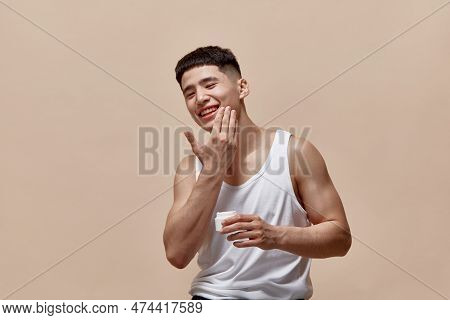 Portrait Of Smiling, Handsome, Young Guy With Clean, Spotless Face Applying Face Moisturizing Cream 