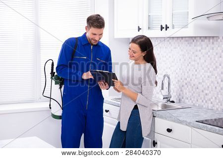 Young Male Pest Control Worker Showing Invoice To Woman In Domestic Kitchen