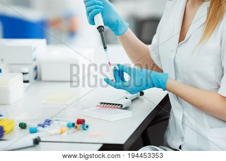 Pipette dropping a sample in a test tube. Laboratory assistant analyzing blood in lab. DNA analysis.