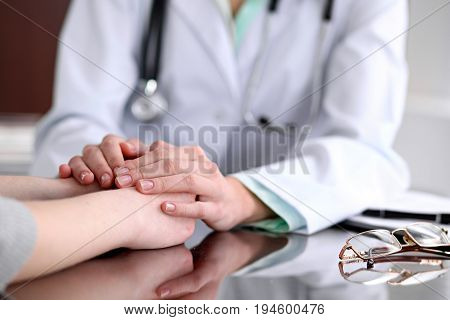 Friendly female doctor hands holding patient hand sitting at the desk for encouragement, empathy, cheering and support while medical examination. Bad news lessening, compassion, trust and ethics concept