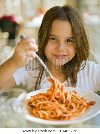 young girl eating spaghetti in restaurant