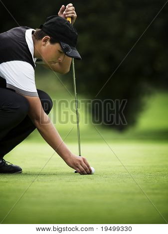 Jogador de golfe jovem de cócoras para colocar a bola no green.