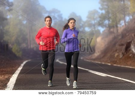 Healthy running runner man and woman workout on mountain road. Jogging male and female fitness model working out training for marathon on forest road in amazing nature landscape. Two runners